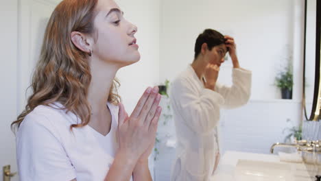 Feliz-Pareja-De-Lesbianas-Caucásicas-Mirándose-En-El-Espejo,-Tocando-El-Cabello-Y-La-Cara-Y-Sonriendo-En-El-Baño