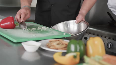 Chef-Masculino-Caucásico-Craping-Verduras-Cortadas-En-Un-Recipiente-En-La-Cocina,-Cámara-Lenta