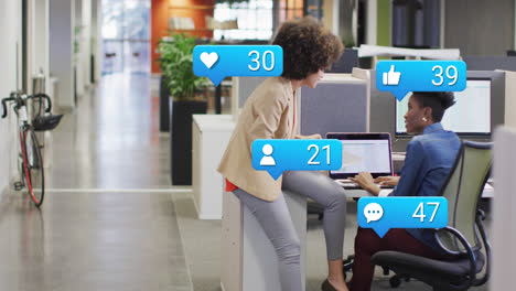 Animation-of-social-media-icons-with-numbers-over-diverse-business-people-using-laptop-at-office