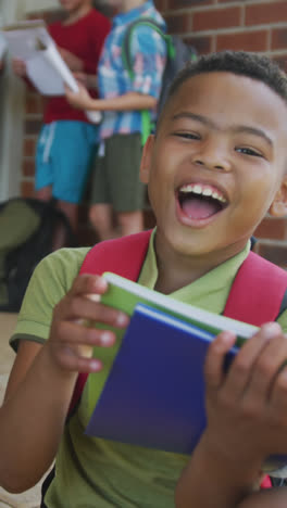 Video-of-happy-african-american-boy-holding-books-in-front-of-school