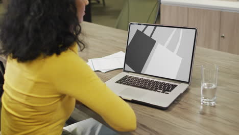 Biracial-woman-at-table-using-laptop,-online-shopping-for-bags,-slow-motion