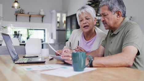 Happy-senior-biracial-couple-talking-and-using-laptop