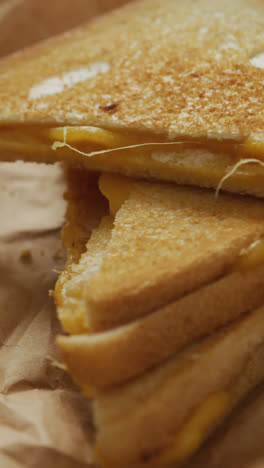 Video-of-close-up-of-toasted-cheese-sandwiches-on-brown-paper-over-grey-background