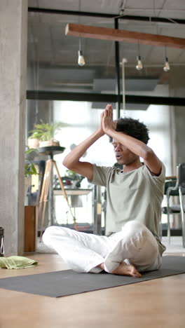 Vertical-video-of-african-american-man-doing-yoga-and-meditating-at-home,-slow-motion