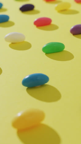 Video-of-overhead-view-of-rows-of-multi-coloured-sweets-over-yellow-background