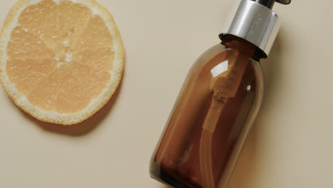 Close-up-of-glass-bottle-with-pump,-lemon-slice-and-copy-space-on-beige-background