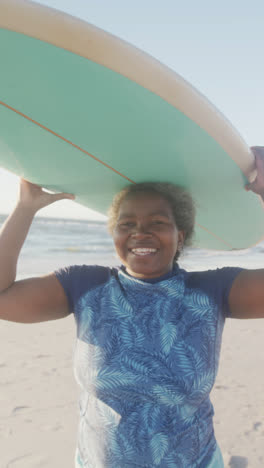 Vertical-video-of-portrait-of-happy-senior-african-american-woman-smiling-at-beach,-in-slow-motion