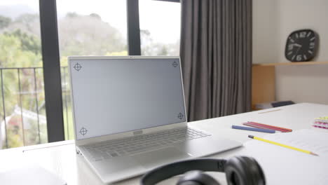 Close-up-of-laptop-with-copy-space-on-screen-and-headphones-on-desk,-slow-motion