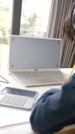 Vertical-video-of-african-american-boy-using-laptop-with-copy-space-on-screen-at-home,-slow-motion