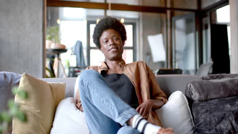 Portrait-of-happy-african-american-man-with-afro-sitting-on-sofa-at-home,-slow-motion