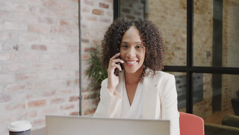 Retrato-De-Una-Feliz-Empresaria-Birracial-Usando-Una-Computadora-Portátil-Y-Hablando-Por-Teléfono-Inteligente,-En-Cámara-Lenta