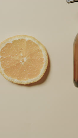 Vertical-video-of-close-up-of-glass-bottle-and-lemon-slice-with-copy-space-on-beige-background