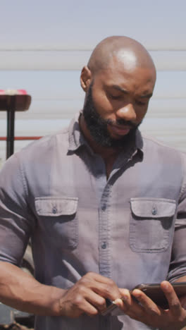 Video-of-african-american-man-standing-with-tablet-in-front-of-tractor