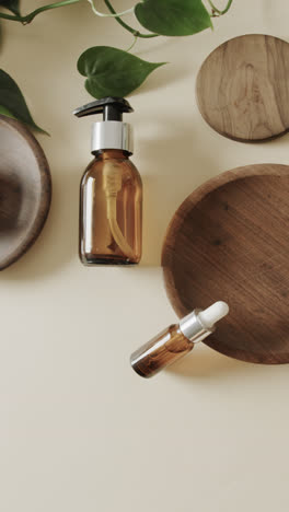 Vertical-video-of-close-up-of-glass-bottles-and-wooden-plates-and-copy-space-on-beige-background