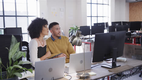 Diverse-male-and-female-colleagues-sitting,-looking-at-computer,-tablet-and-talking,-slow-motion