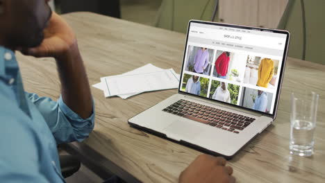 Hombre-Afroamericano-En-La-Mesa-Usando-Laptop,-Comprando-Ropa-En-Línea,-Cámara-Lenta