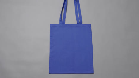 Primer-Plano-De-Una-Bolsa-Azul-Sobre-Fondo-Gris,-Con-Espacio-Para-Copiar,-Cámara-Lenta