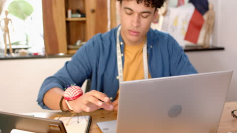 Biracial-male-fashion-designer-sketching-design-at-desk-on-laptop-in-studio,-slow-motion