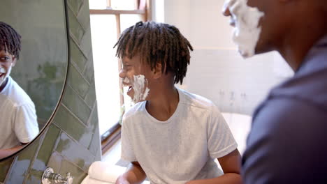 Feliz-Padre-E-Hijo-Afroamericanos-Aplicando-Espuma-De-Afeitar-En-La-Cara-En-El-Baño-De-Casa,-Cámara-Lenta