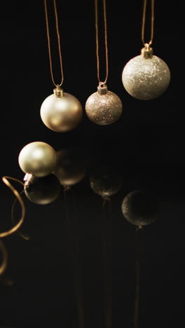 Vertical-video-of-gold-baubles-christmas-decorations-and-copy-space-on-black-background