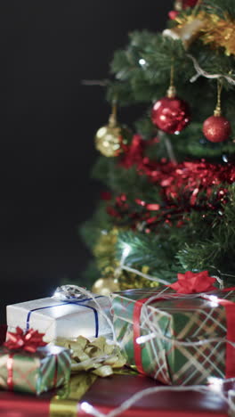 Vertical-video-of-christmas-tree-with-presents-and-decorations-and-copy-space-on-black-background