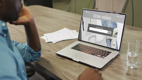 African-american-man-at-table-using-laptop,-online-shopping-for-clothes-and-accessories,-slow-motion