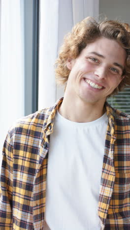 Vertical-video-of-portrait-of-happy-caucasian-man-looking-through-window-at-home,-slow-motion