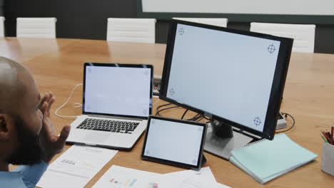 African-american-businessman-using-computer,-tablet-and-laptop,-copy-space-on-screens,-slow-motion