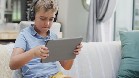 Happy-caucasian-boy-sitting-on-sofa-and-using-tablet,-slow-motion