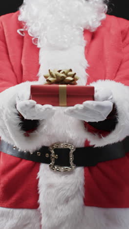 Vertical-video-of-santa-claus-holding-christmas-present-with-copy-space