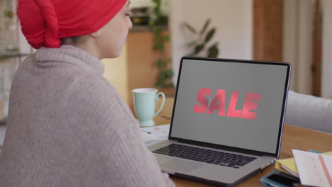 Biracial-woman-at-table-using-laptop,-online-shopping-during-sale,-slow-motion