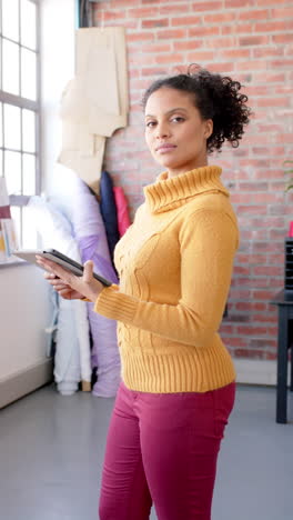 Feliz-Y-Diversa-Diseñadora-De-Moda-Femenina-Parada-Y-Sosteniendo-Una-Tableta-En-El-Estudio,-Cámara-Lenta,-Vertical