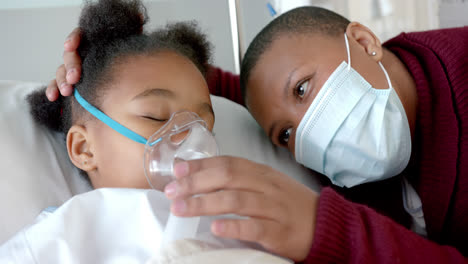 Mujer-Afroamericana-Con-Mascarilla-Acariciando-A-Su-Hija-Con-Máscara-De-Oxígeno-En-El-Hospital,-Cámara-Lenta