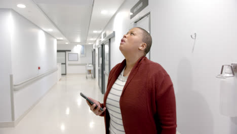 Mujer-Afroamericana-Estresada-Usando-Un-Teléfono-Inteligente-En-El-Pasillo-Del-Hospital,-Cámara-Lenta