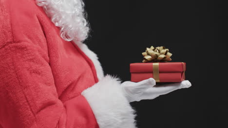 Video-of-santa-claus-holding-christmas-present-with-copy-space-on-black-background