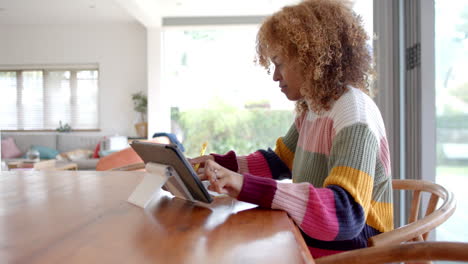 African-american-woman-sitting-at-table-and-using-tablet,-slow-motion