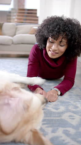 Vertical-video-of-biracial-woman-playing-with-dog-on-floor-at-home,-slow-motion