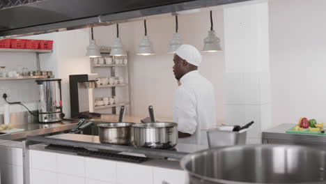 African-american-male-chef-using-tablet-and-talking-on-smartphone-in-kitchen,-slow-motion