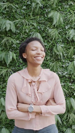 Vertical-video-of-portrait-of-happy-african-american-businesswoman-over-plants-in-slow-motion