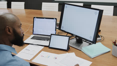 African-american-businessman-using-computer,-tablet-and-laptop,-copy-space-on-screens,-slow-motion