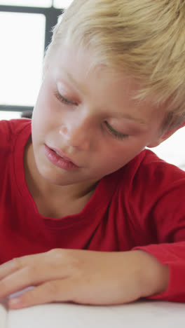 Video-of-happy-caucasian-boy-sitting-at-school-desk-and-writing