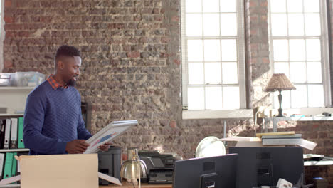 Happy-african-american-casual-businessman-holding-images-in-creative-office-in-slow-motion