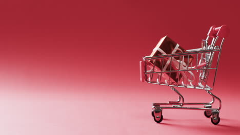 Video-of-shopping-trolley-with-christmas-gift-and-copy-space-on-red-background