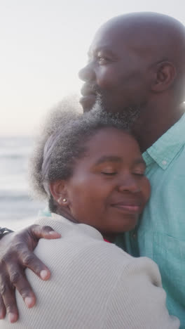 Video-Vertical-De-Una-Pareja-Afroamericana-Mayor-Abrazándose-En-La-Playa,-En-Cámara-Lenta