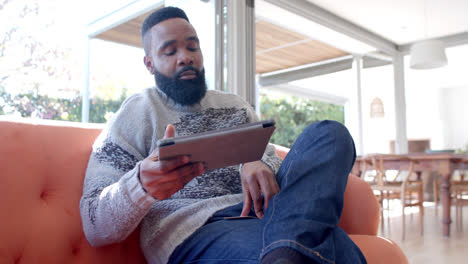 African-american-man-using-tablet-and-credit-card-in-sunny-living-room,-slow-motion