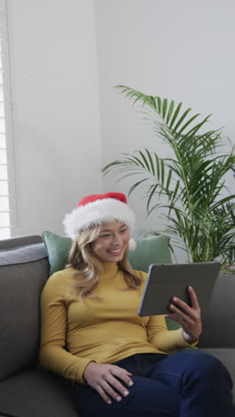 Vertical-video-of-biracial-woman-wearing-santa-hat-using-tablet-for-video-call,-slow-motion