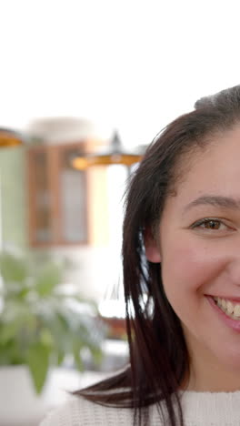 Vertical-video-of-half-face-of-happy-biracial-woman-with-straight-hair-smiling-in-sunny-kitchen