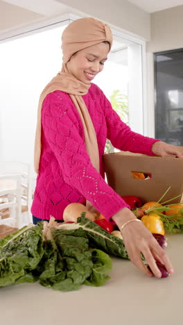 Video-Vertical-De-Una-Mujer-Birracial-Con-Hijab-Preparando-Comida-En-La-Cocina-De-Casa,-Espacio-Para-Copiar,-Cámara-Lenta