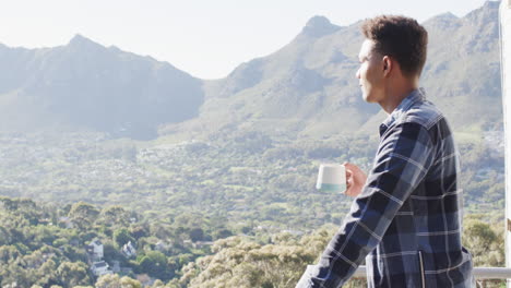 Hombre-Afroamericano-Tomando-Café-En-El-Balcón-Con-Vistas-Soleadas-A-La-Montaña,-Espacio-Para-Copiar,-Cámara-Lenta