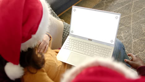 Feliz-Pareja-Diversa-Con-Sombreros-Navideños-Usando-Una-Computadora-Portátil-Con-Pantalla-De-Espacio-De-Copia,-Cámara-Lenta